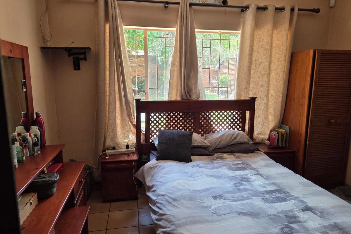 A bedroom featuring tiled flooring, a large window with security bars, and built-in wooden cabinetry.
