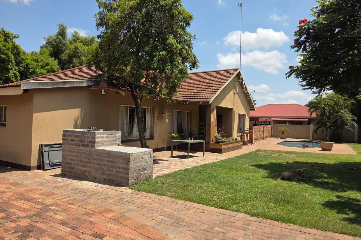 Rear view of the property featuring a paved patio area, built-in brick braai, swimming pool, and a spacious garden.