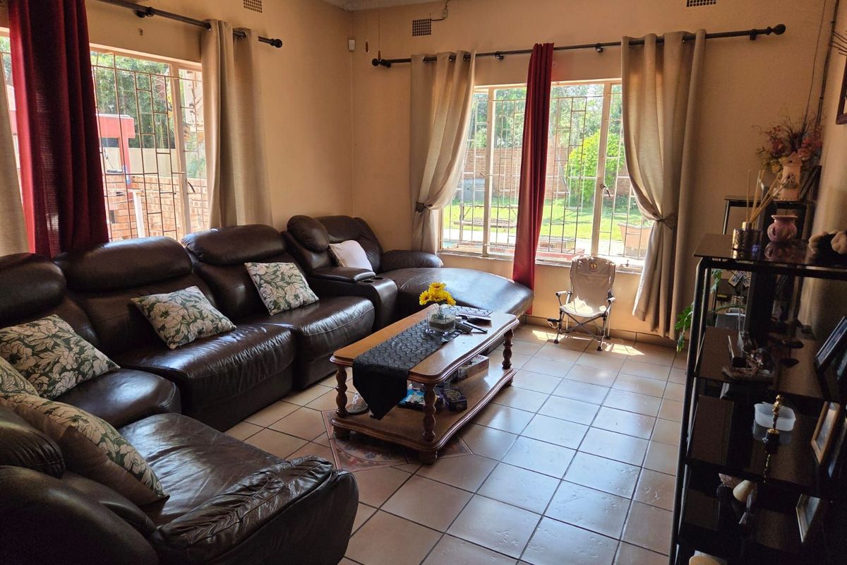 A spacious living room featuring large windows with security bars, tiled flooring, and a wall-mounted air conditioning unit.