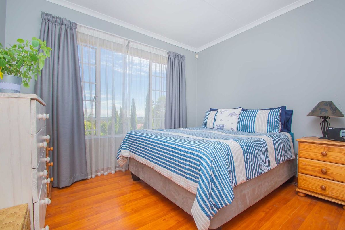 A well-maintained bedroom featuring warm timber flooring, large windows with natural light, and neutral wall finishes.