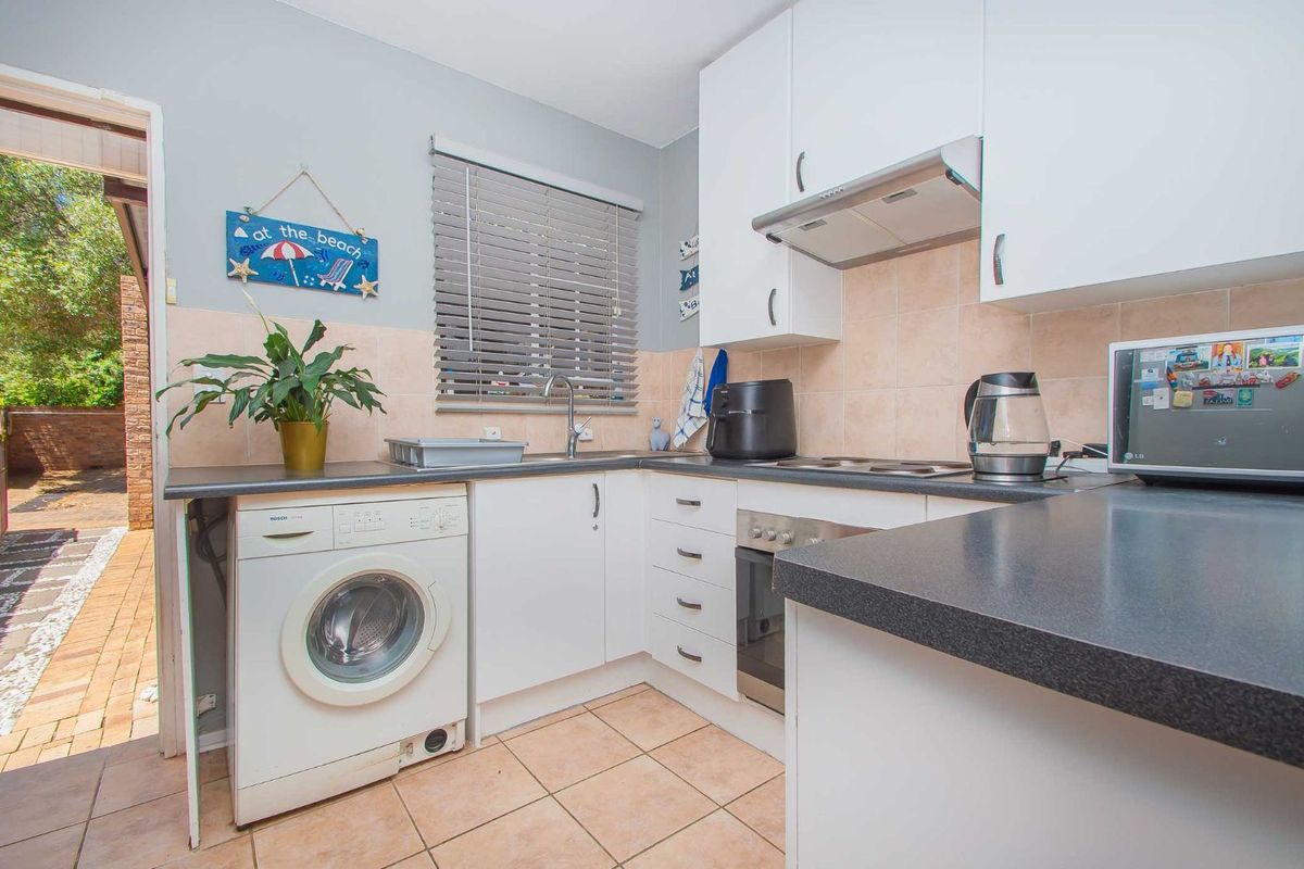 Compact kitchen featuring white cabinetry, integrated oven, hob, extractor fan, and built-in laundry plumbing, with direct access to an outdoor patio area.
