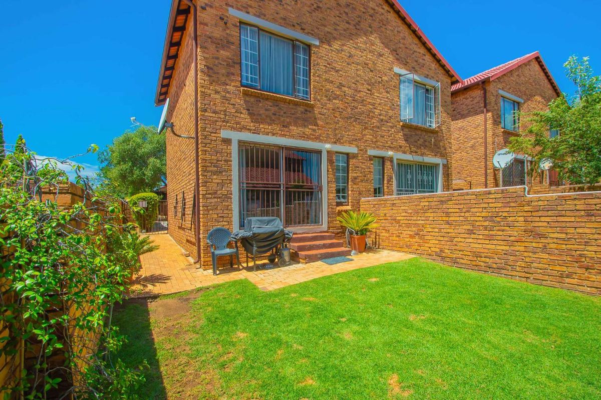 A private rear garden featuring a paved patio area, established lawn, and brick boundary walls, providing a functional outdoor space for the home.