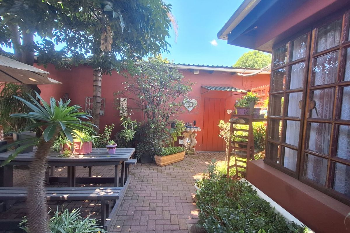 A private rear courtyard featuring paved flooring, established garden greenery, and direct access to the home through timber-framed windows.
