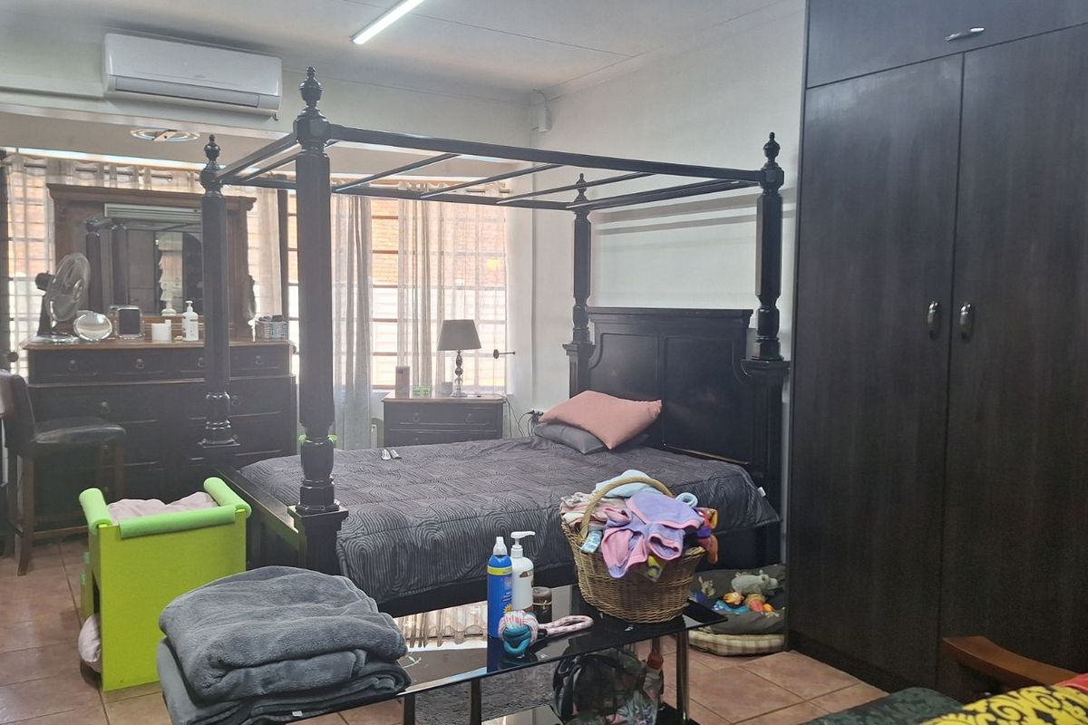 A spacious bedroom featuring built-in dark wood cabinetry, tiled flooring, and a wall-mounted air conditioning unit.