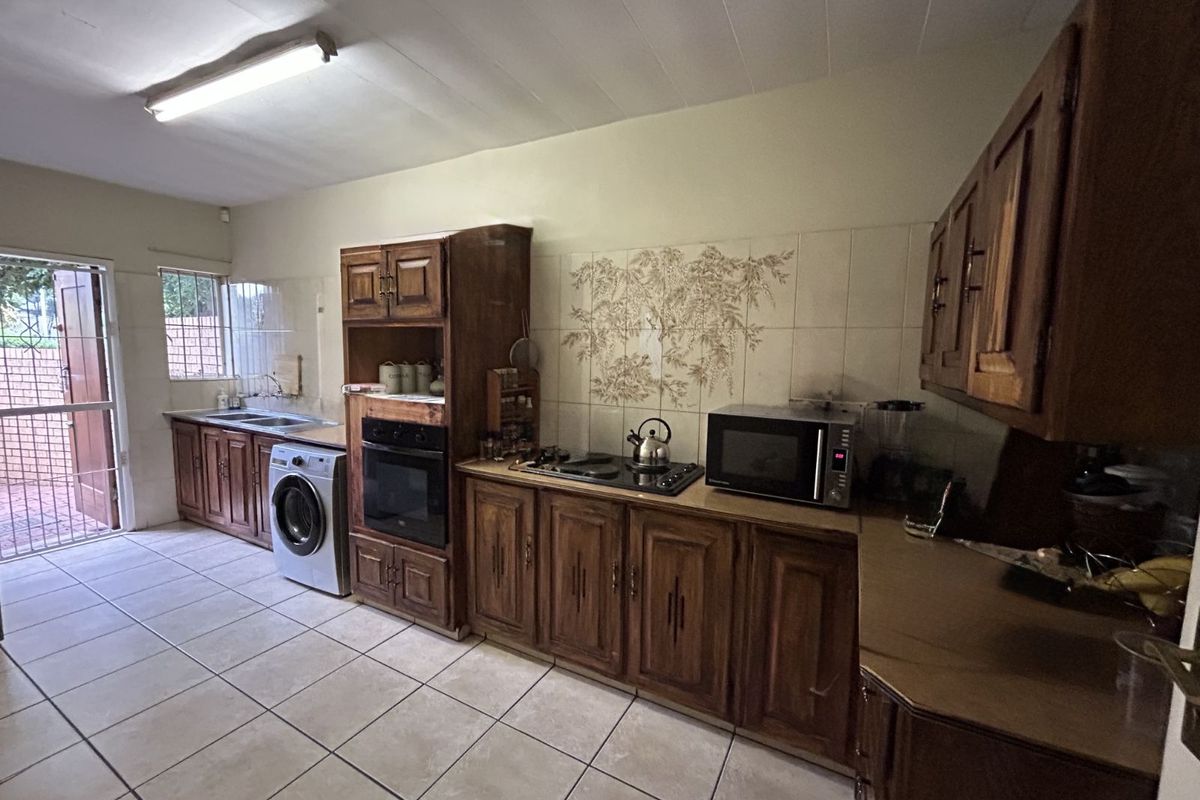 A functional kitchen featuring wooden cabinetry, tiled flooring, a built-in oven, and a hob, with direct access to an outdoor area.