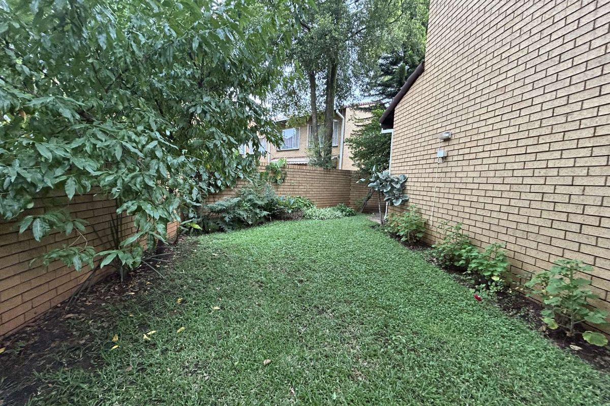 A private rear garden area featuring a manicured lawn, established trees, and perimeter brick boundary walls.
