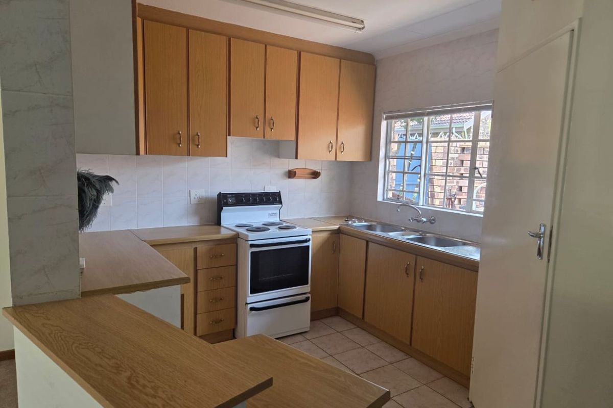 A functional kitchen featuring wooden cabinetry, tiled flooring, a double sink, and a freestanding electric stove with an oven.