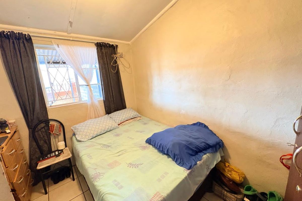 A compact bedroom featuring tiled flooring, a window with security bars, and basic wall finishes.