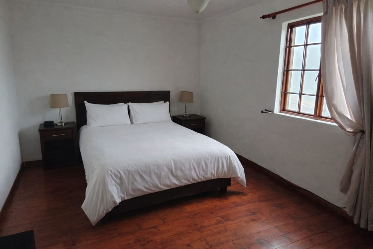 A simple bedroom featuring dark wood flooring and a window with wooden frames.