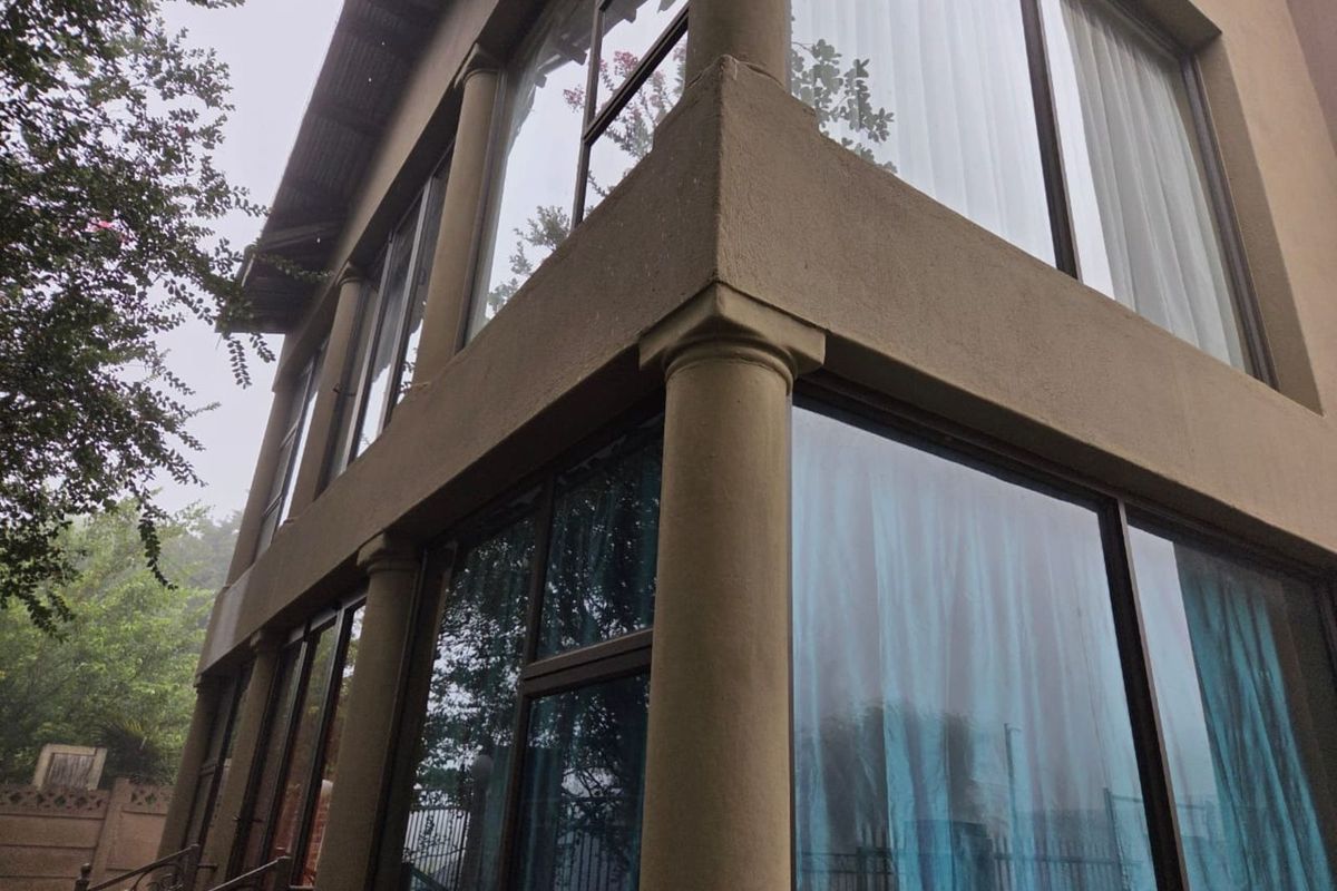 A two-story exterior view of the property featuring large glass windows, structural columns, and a covered balcony area.