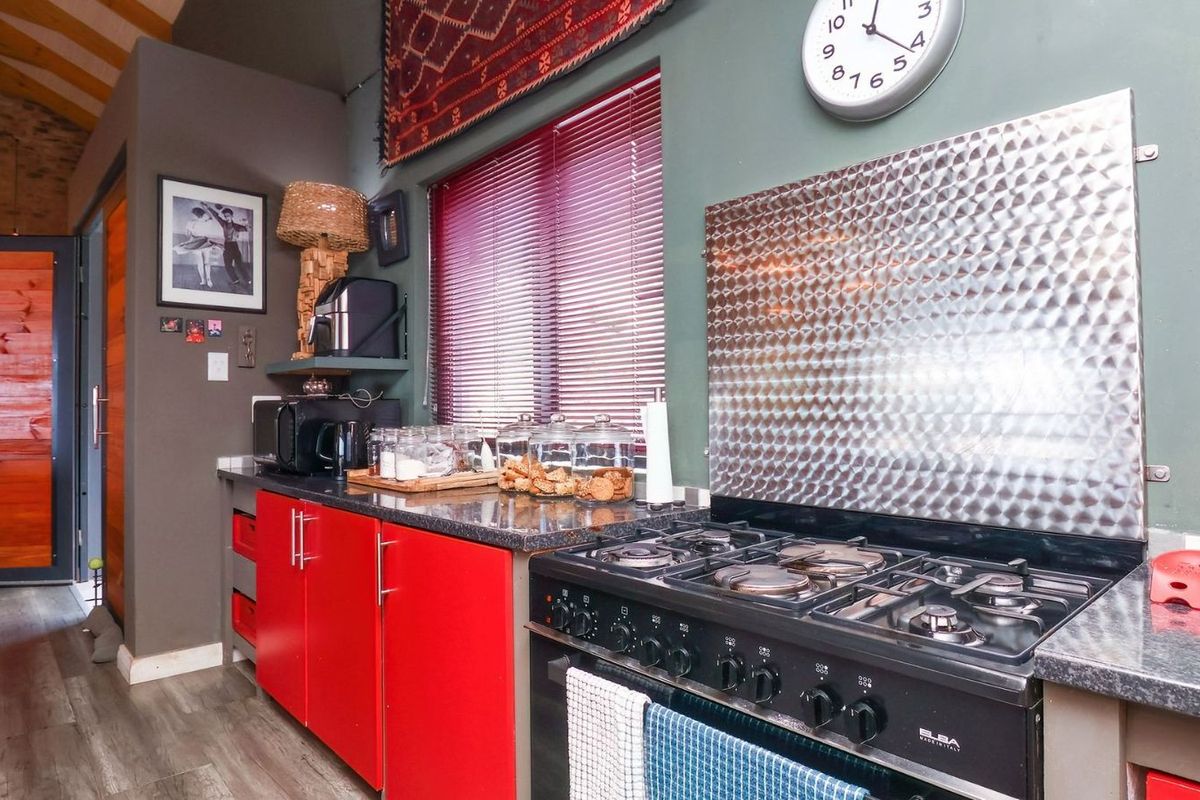 A kitchen area featuring a gas stove with a stainless steel splashback, dark granite countertops, and vibrant red cabinetry.