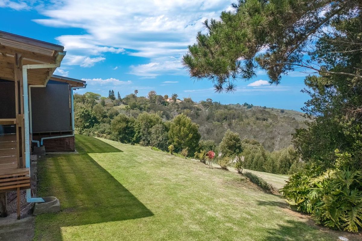 A scenic view of the rear garden and surrounding landscape, featuring a covered timber deck and well-maintained lawn.