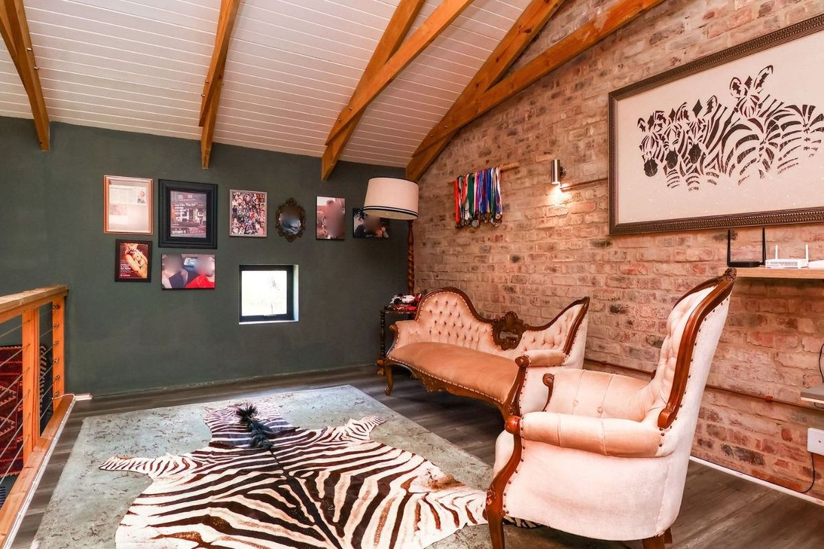 A cozy living area featuring exposed brick walls, vaulted ceilings with timber beams, and a mezzanine-style layout overlooking the lower level.