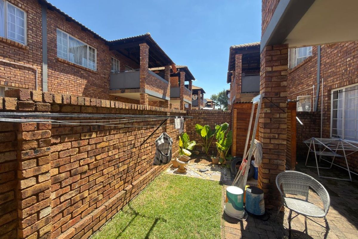 A private rear courtyard featuring a small lawn, brick boundary walls, and paved patio area within a multi-unit residential complex.