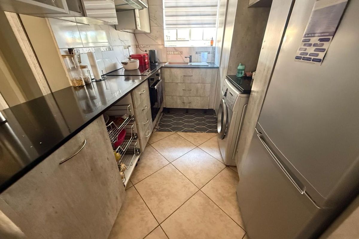 Compact galley-style kitchen featuring stone-look cabinetry, dark countertops, integrated sink, and dedicated space for laundry appliances.