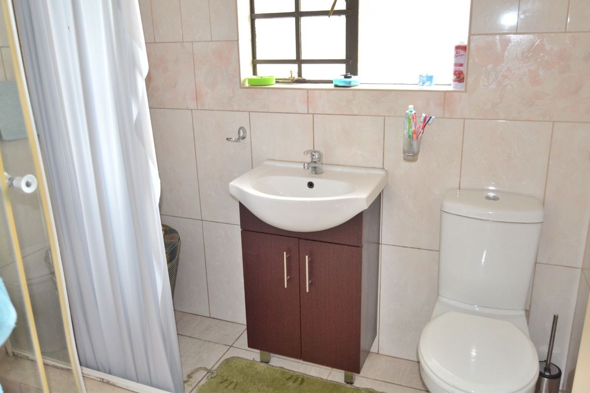 A functional bathroom featuring a vanity basin, a toilet, and a shower area with tiled walls and flooring.