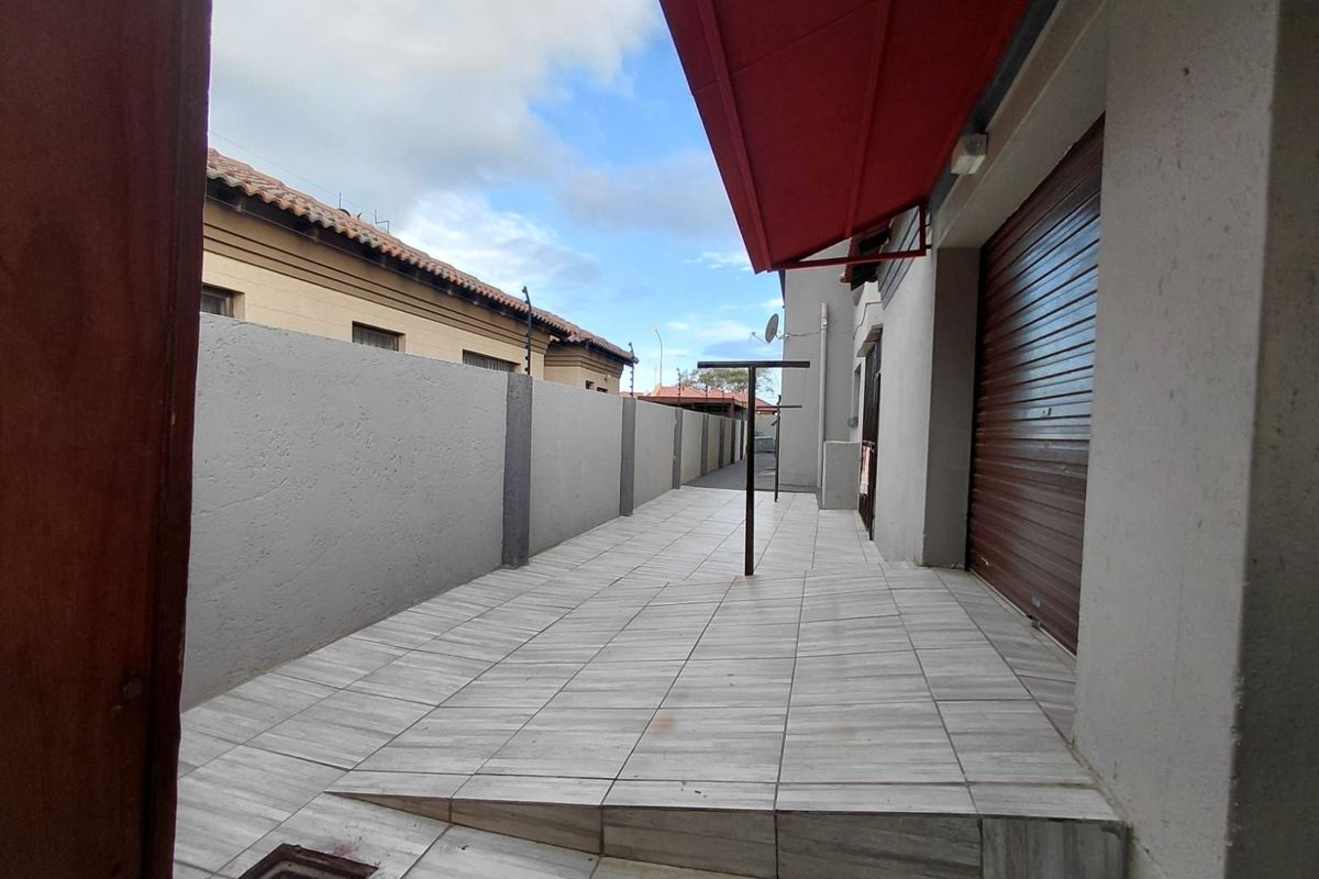 A paved side exterior area featuring a retractable red awning, a metal security roller shutter, and a built-in accessibility ramp.