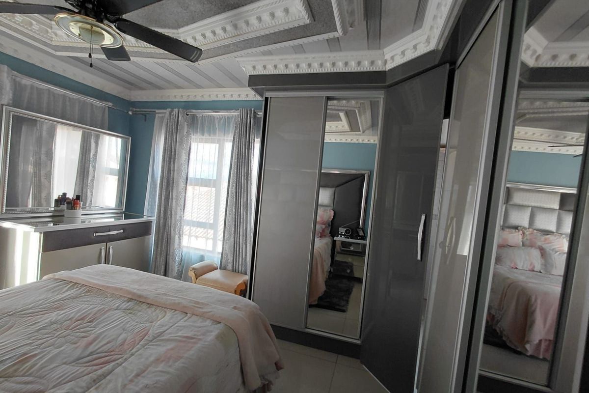 A bedroom featuring built-in mirrored wardrobes, decorative ceiling molding, and a ceiling fan.