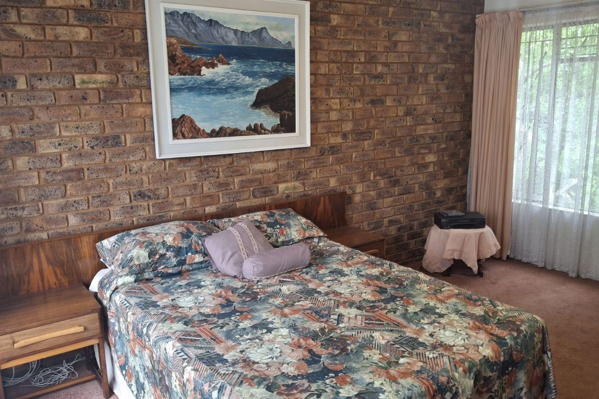 A bedroom featuring a prominent face-brick feature wall, carpeted flooring, and large window with curtains.