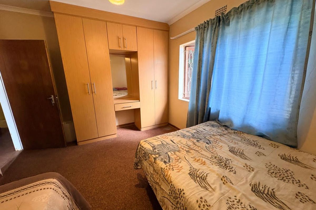 A bedroom featuring built-in wooden cabinetry with a vanity section, carpeted flooring, and a window with security bars.