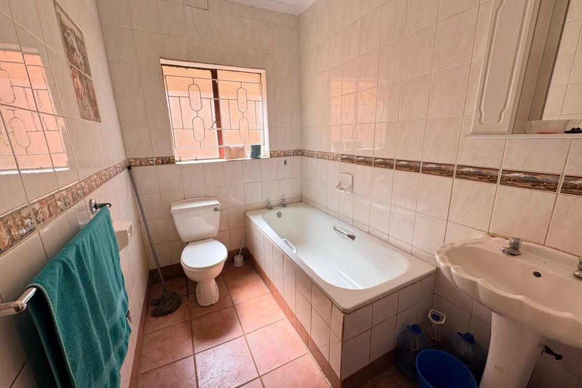 A functional bathroom featuring a standard bathtub, pedestal basin, and toilet, finished with ceramic wall and floor tiling.