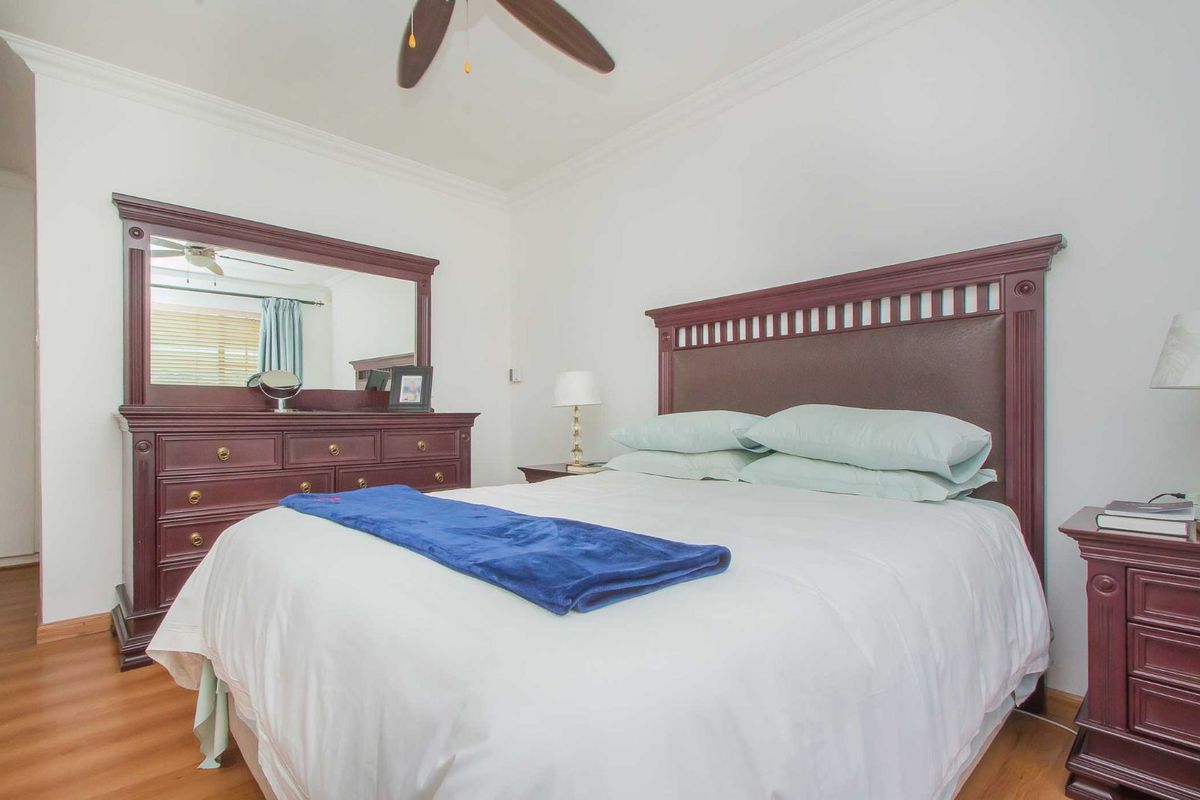 A well-maintained bedroom featuring laminate flooring, crown molding, and a ceiling fan.