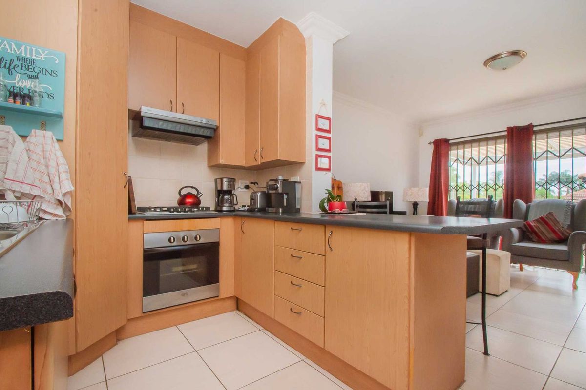 A functional kitchen featuring light wood cabinetry, a built-in oven, gas hob, extractor fan, and a breakfast bar counter overlooking the living area.