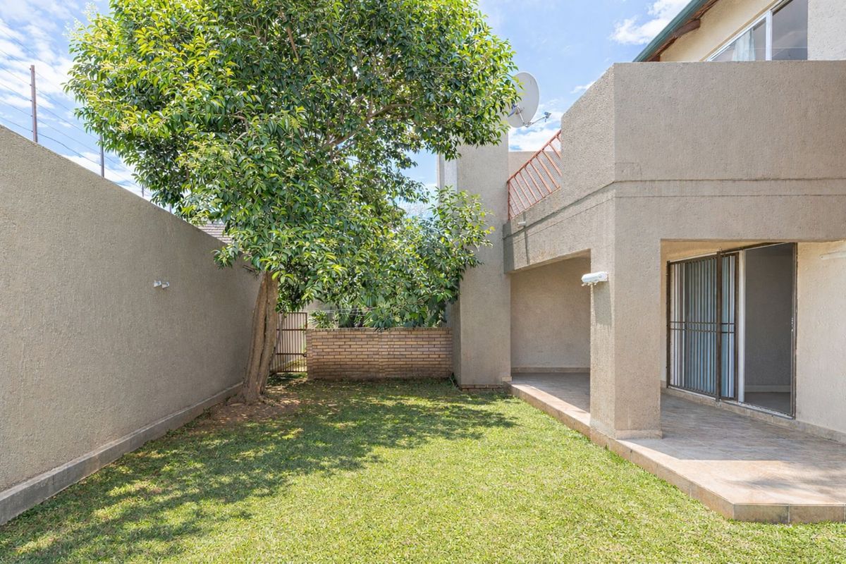A private rear garden featuring a paved patio area, established tree, and a secure boundary wall, providing a quiet outdoor space.