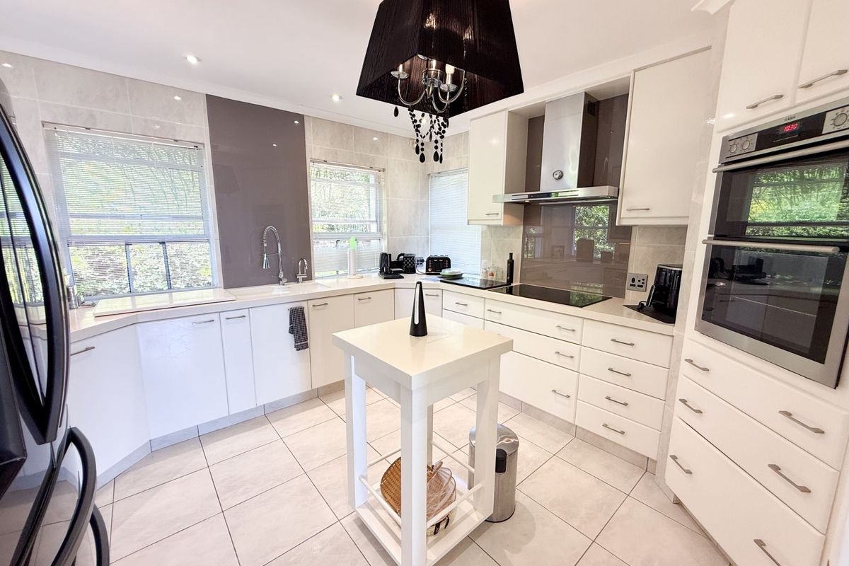 Modern kitchen featuring white cabinetry, stone countertops, integrated oven, glass cooktop, and a central island, finished with tiled flooring and neutral splashbacks.