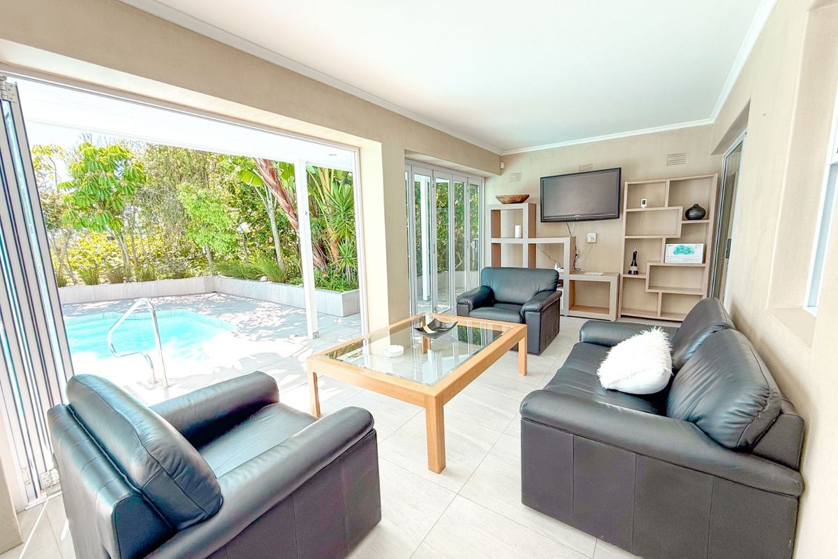Bright living room featuring large sliding glass doors that open directly onto a private swimming pool and garden area.