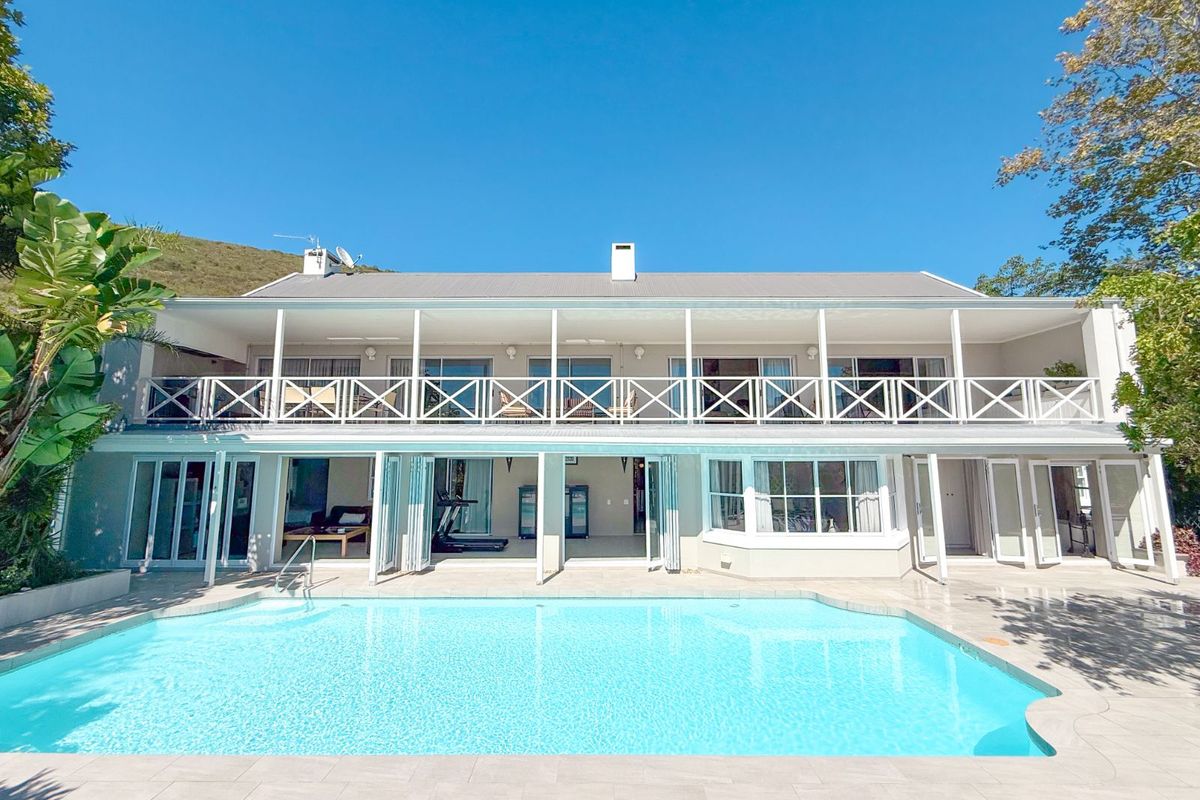 A spacious rear exterior view featuring a large swimming pool, a covered patio area, and a two-story facade with a balcony and folding glass doors.