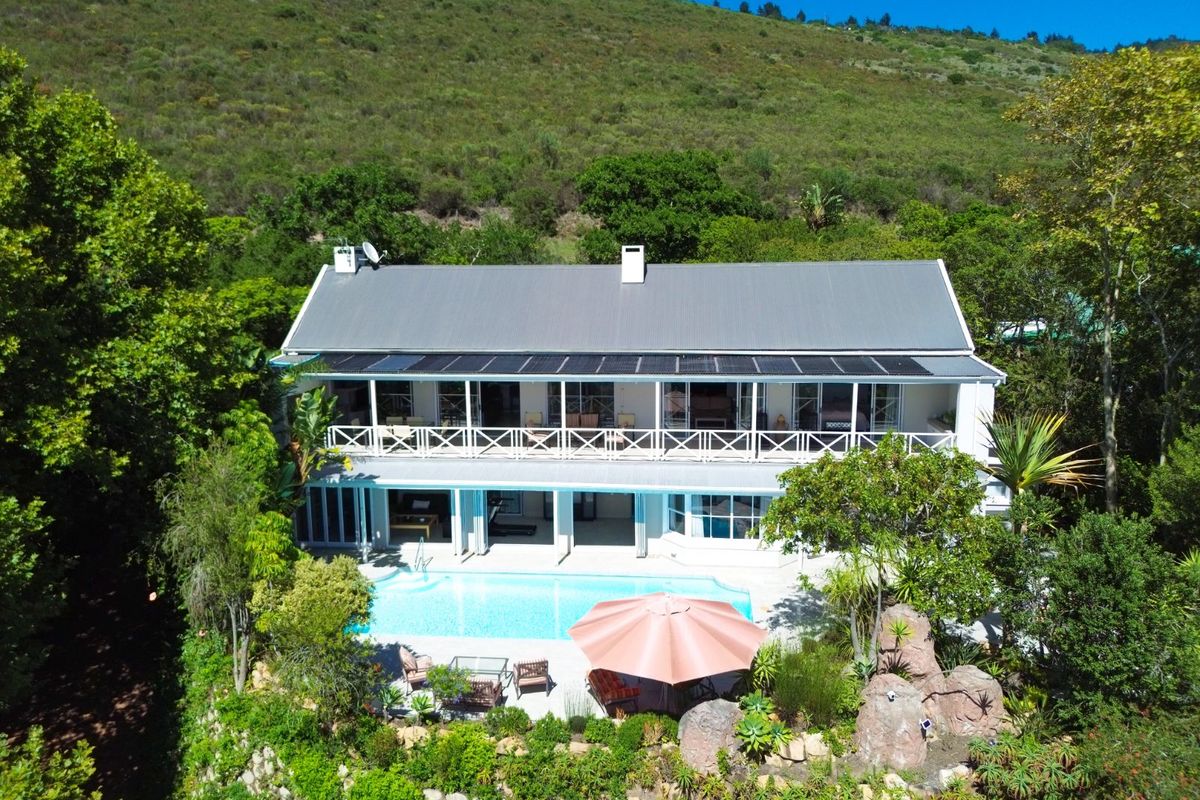 Aerial view of a two-story residence featuring a swimming pool, expansive rear patio, balcony, and solar panels set against a lush mountain backdrop.