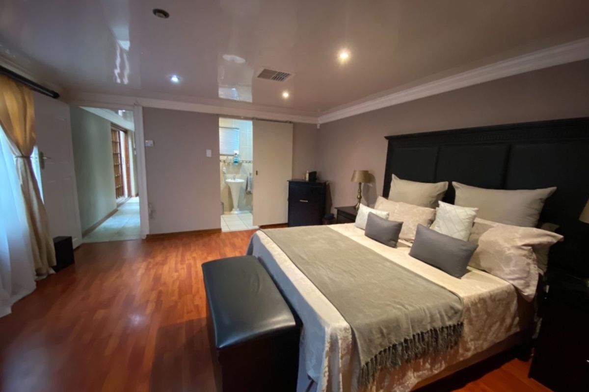 Spacious bedroom featuring warm-toned laminate flooring, recessed ceiling lighting, and an en-suite bathroom access.