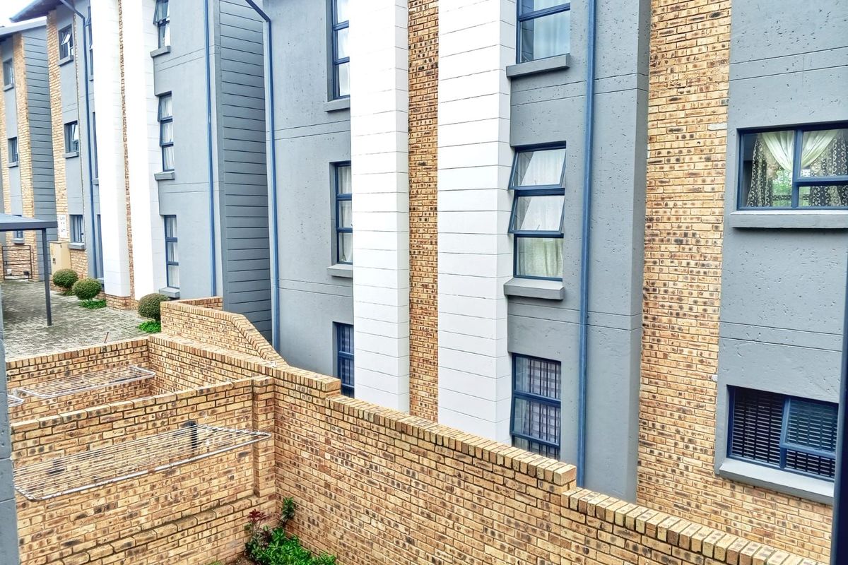 A view of the apartment building exterior featuring face brick and painted concrete facade with aluminium window frames and a low brick boundary wall.