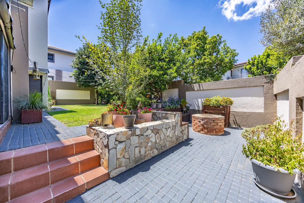 A well-maintained rear garden featuring paved patio areas, a stone-clad retaining wall, a brick fire pit, and established landscaping.