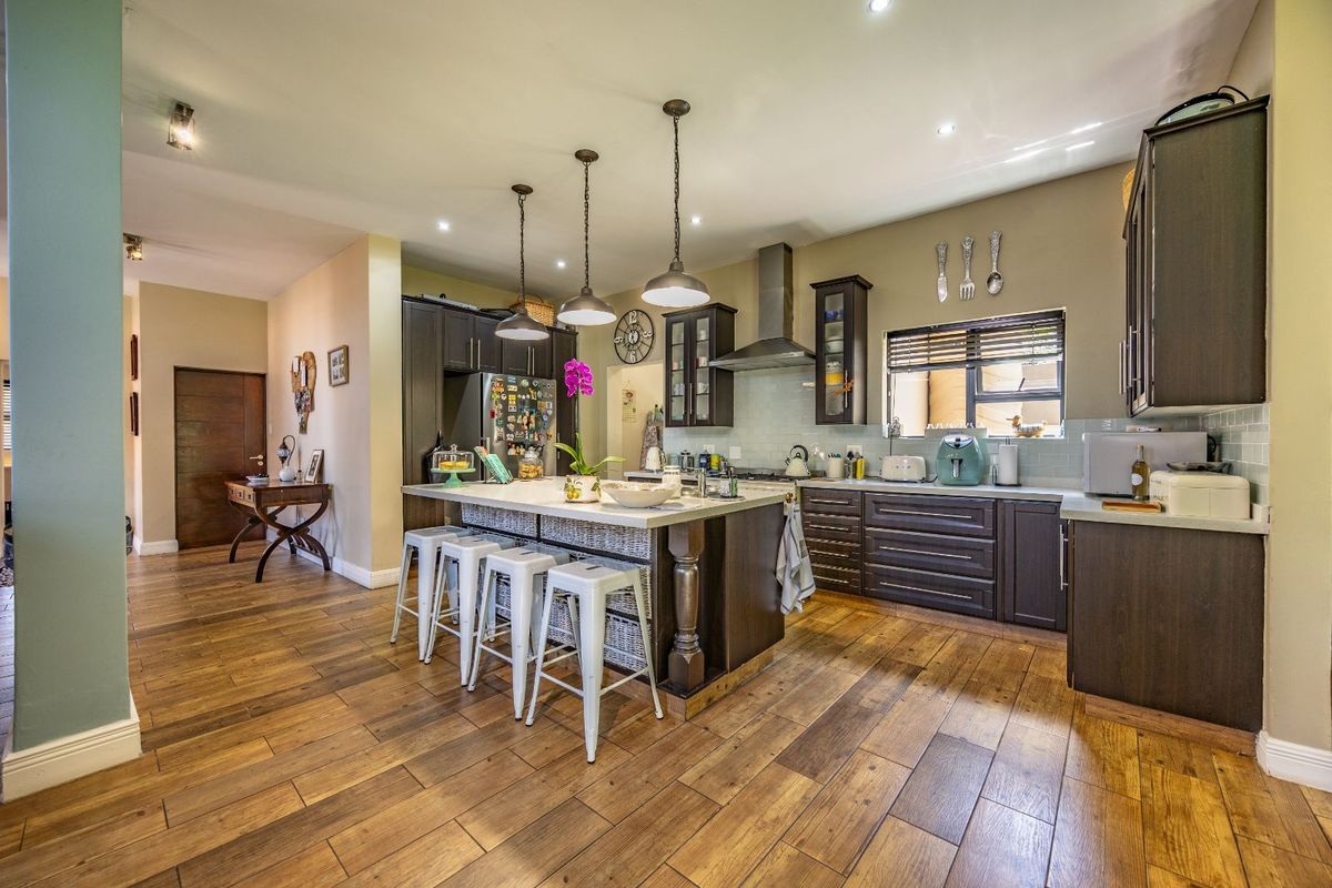 Spacious kitchen featuring dark cabinetry, a central island with breakfast bar seating, stainless steel extractor fan, and durable wood-look flooring throughout.