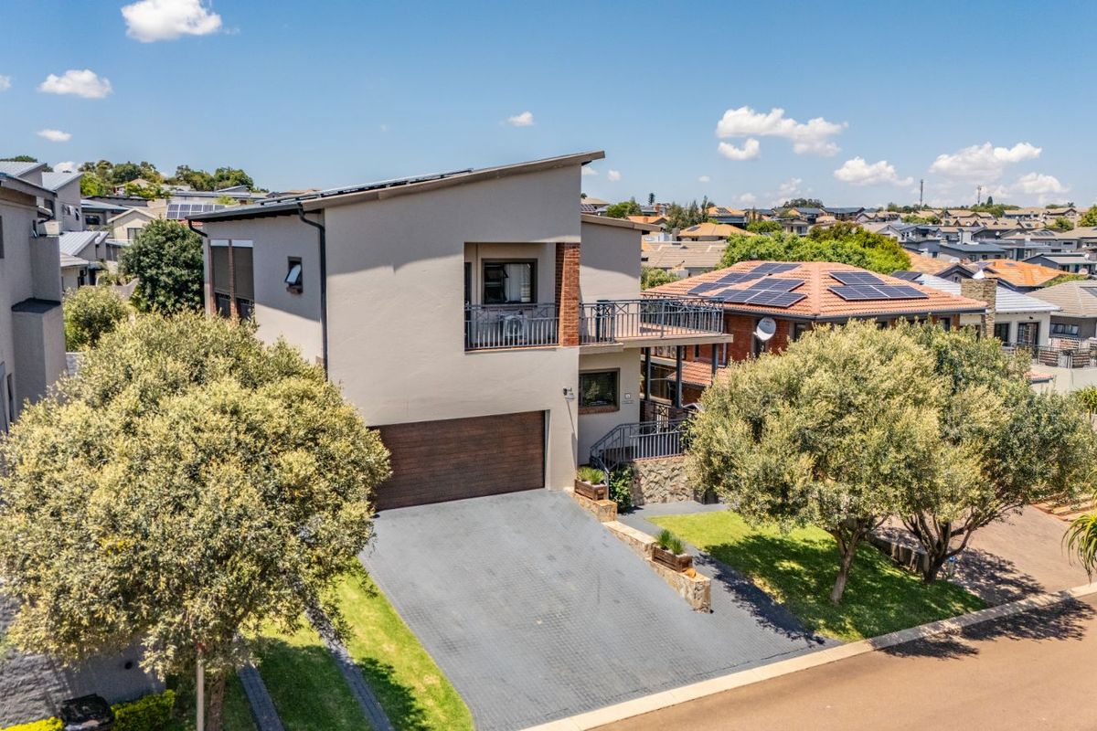 Aerial view of a modern double-story residential property featuring a paved driveway, integrated garage, and a balcony overlooking the surrounding suburban neighborhood.