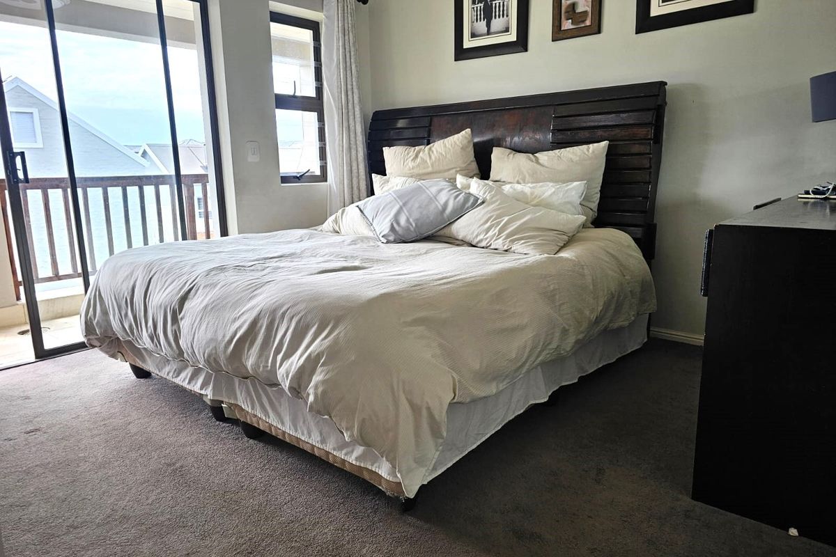 A comfortable bedroom featuring carpeted flooring, a large window, and sliding glass doors that provide access to an outdoor balcony area.