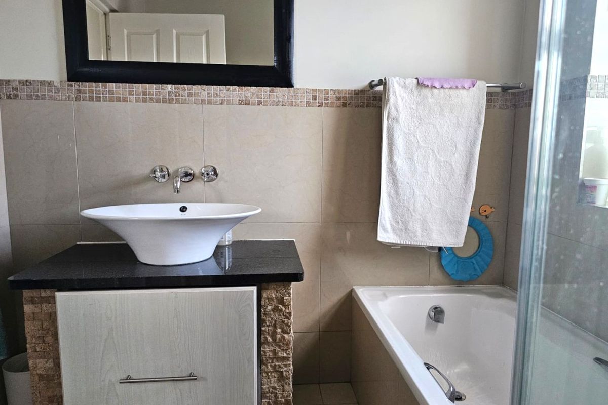 A functional bathroom featuring a vessel sink on a granite vanity, a built-in bathtub, and neutral wall tiling.