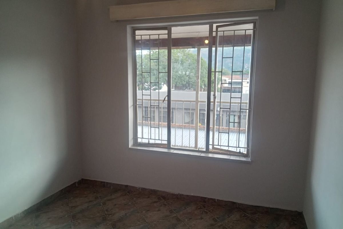 A vacant bedroom featuring tiled flooring and a large window with integrated security bars, offering natural light and an exterior view.