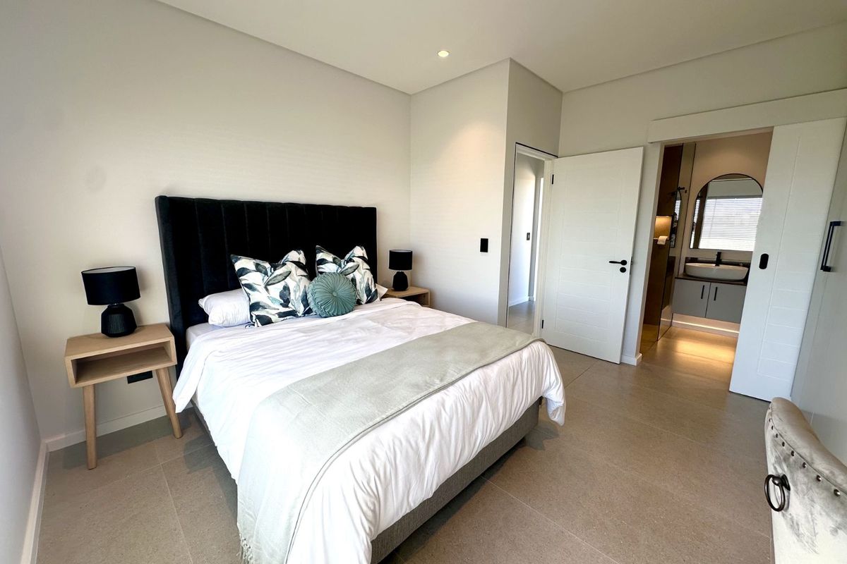 Modern bedroom featuring neutral tiled flooring, recessed downlighting, and an en-suite bathroom accessible via a sliding door.