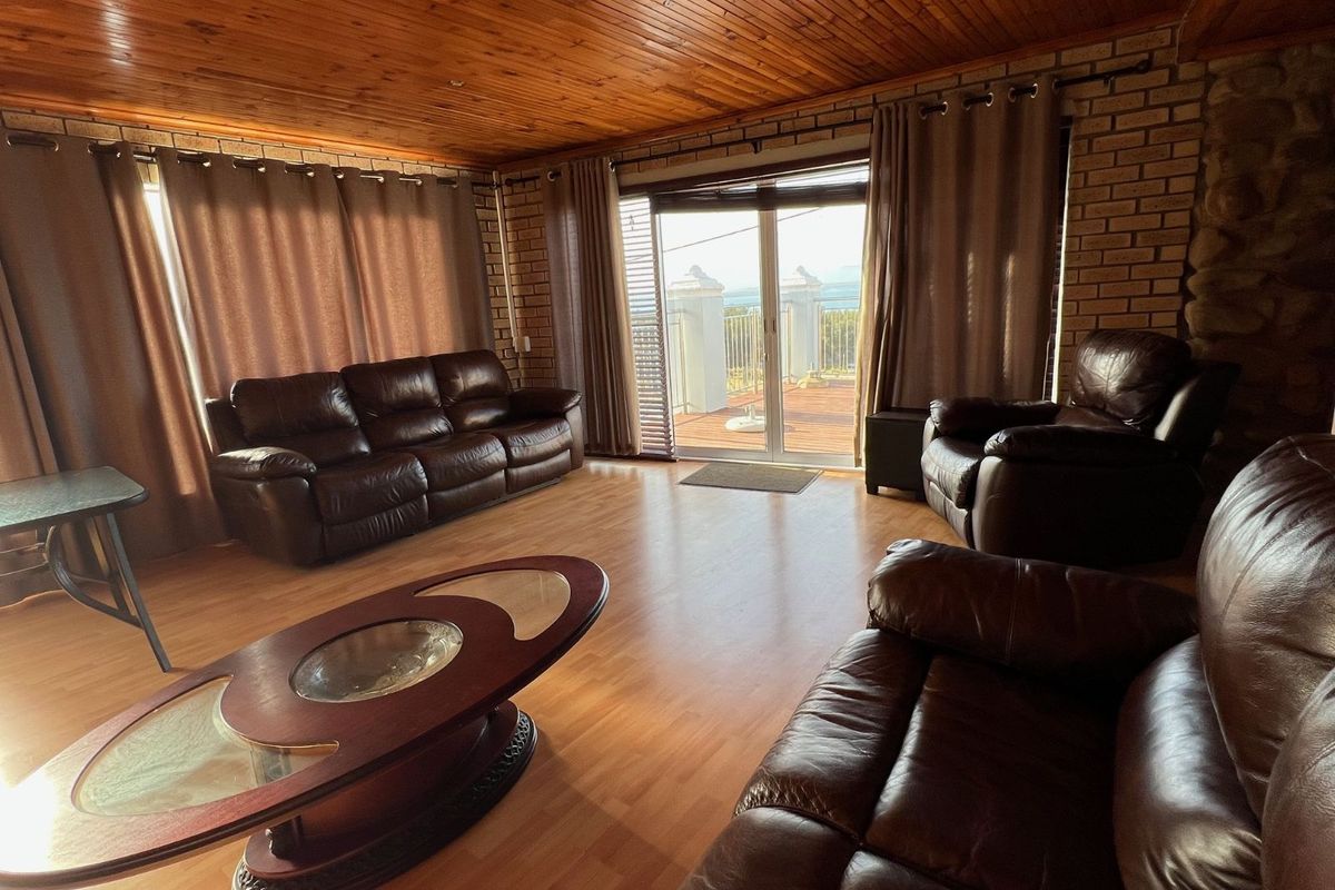 Spacious living room featuring a timber-clad ceiling, exposed brick walls, laminate flooring, and sliding glass doors leading to an outdoor balcony with scenic views.