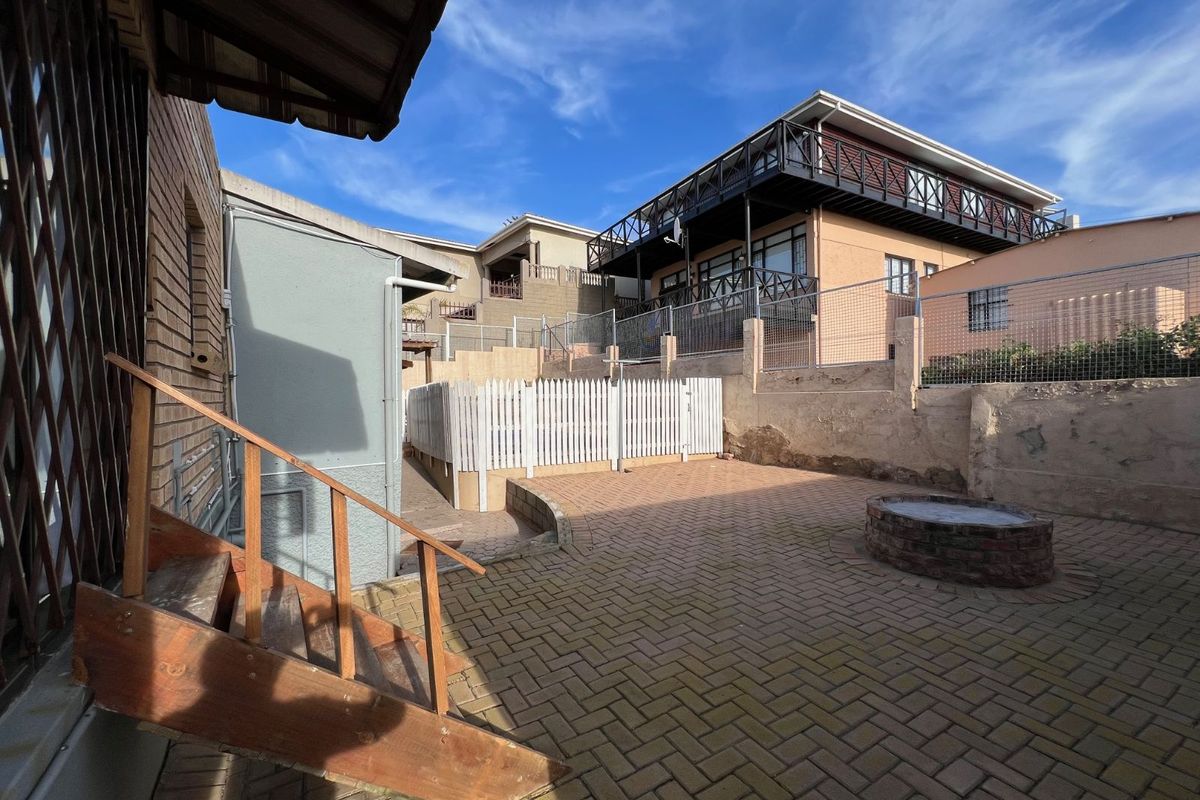 A paved rear courtyard area featuring a brick fire pit, wooden staircase, and perimeter fencing, offering a functional outdoor space for the property.