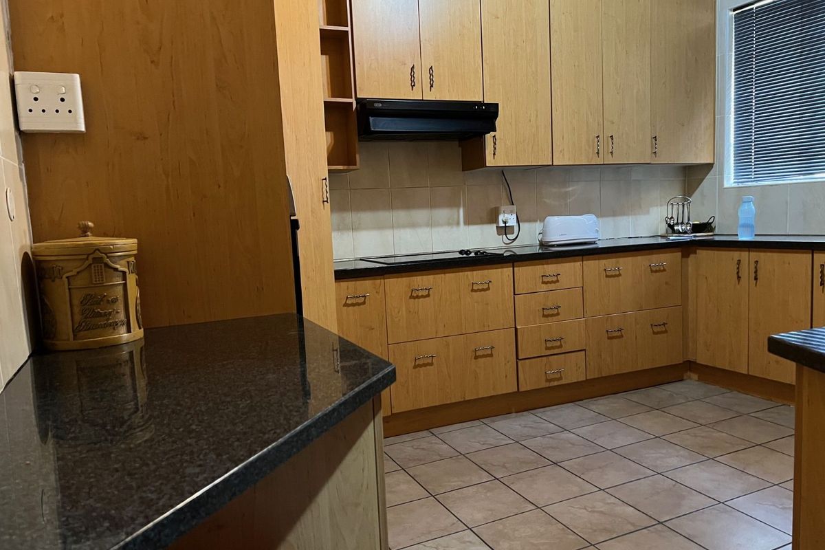 A functional kitchen featuring light wood cabinetry, dark granite countertops, tiled flooring, and a built-in extractor fan.