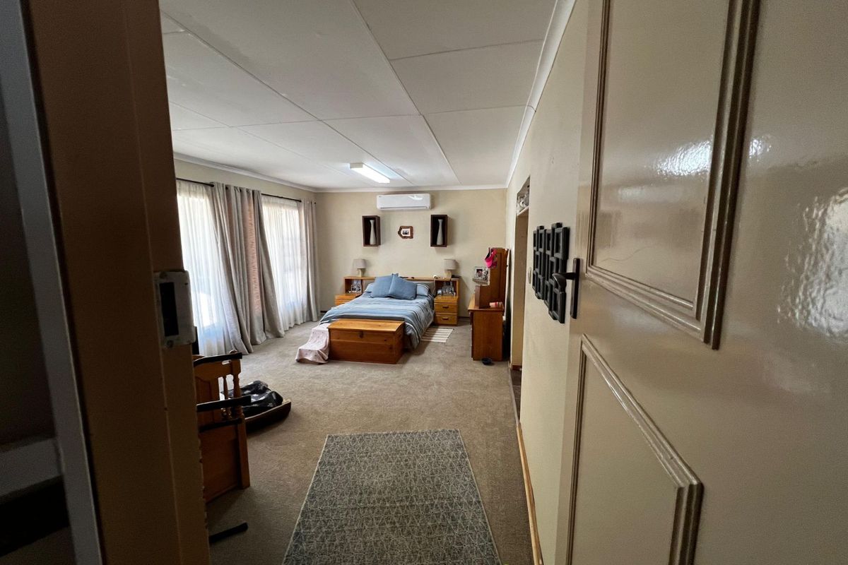 Spacious bedroom featuring neutral walls, carpeted flooring, and a wall-mounted air conditioning unit.
