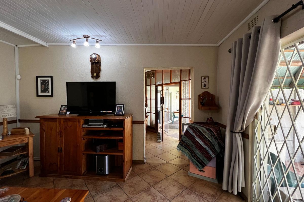 A living room featuring tiled flooring, a timber-paneled ceiling, and a glass-paneled door leading to an adjacent room, with security gate access to the exterior.