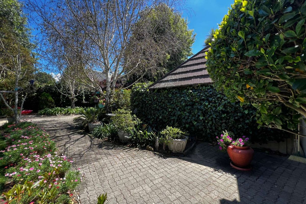 A well-maintained rear garden area featuring paved pathways, mature trees, and established landscaping surrounding the property.