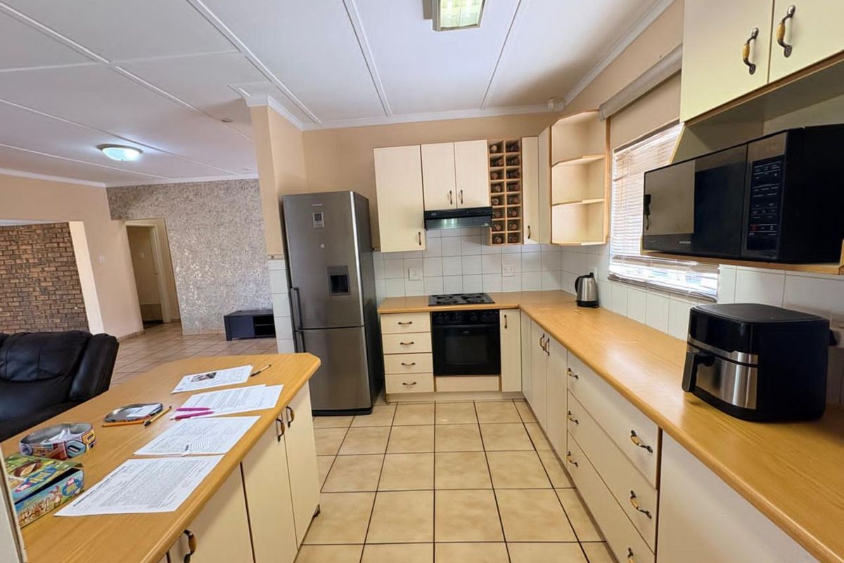 A functional kitchen featuring light-toned cabinetry, laminate countertops, built-in oven, hob, and extractor fan, with tiled flooring throughout.