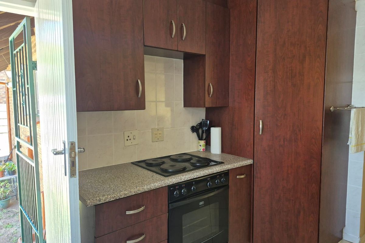 A compact kitchen featuring dark wood cabinetry, a built-in oven, a four-plate electric hob, and tiled splashbacks.