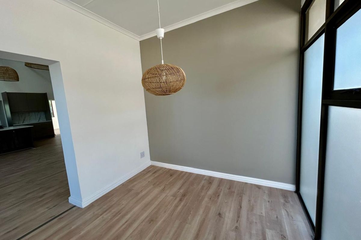 A bright, empty room featuring modern wood-look laminate flooring, a neutral accent wall, and a contemporary pendant light fixture.